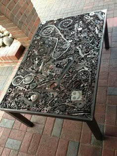 a table that is made out of gears and other things on the ground next to a brick wall