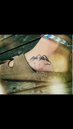 a woman's foot with a mountain tattoo on her left ankle and the mountains behind her