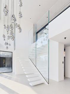 a white staircase with glass railing and chandelier hanging from it's ceiling