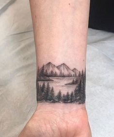 a person's hand with a tattoo on it that has trees and mountains in the background