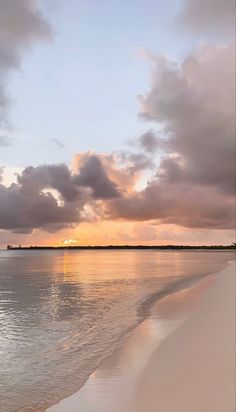 the sun is setting over the water at the beach with clouds in the sky and sand on the shore