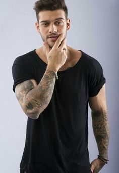 a man with tattoos on his arm posing for the camera while holding his hand to his face