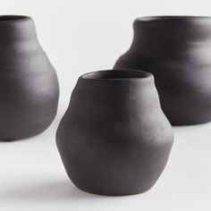 three black vases sitting next to each other on a white surface with no one around them