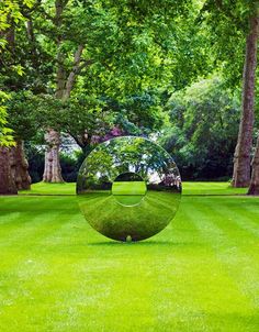 a large metal sculpture sitting in the middle of a lush green field next to trees