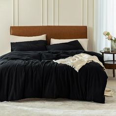 a bed with black sheets and pillows in a white room next to a small table