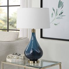 a blue vase sitting on top of a glass table next to a white lamp shade