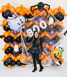 a woman standing in front of balloons and decorations for an halloween party with boos