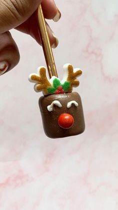 a hand holding a small christmas decoration on top of a piece of chocolate with reindeer's nose