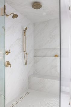 a walk in shower sitting next to a white tiled wall with gold faucets