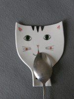 a white cat shaped plate with a spoon in it's mouth and eyes painted on the side