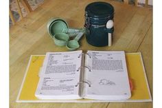 an open book sitting on top of a wooden table next to cups and utensils