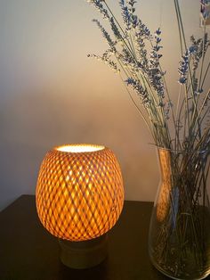 two vases with flowers in them sitting on a table next to a lamp that is turned on