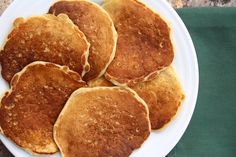 four pancakes on a white plate sitting on top of a green tablecloth next to a knife and fork