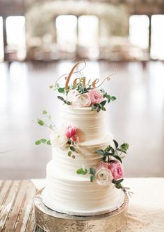 a white wedding cake with pink flowers and the word love on top is sitting on a table