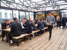 a group of people sitting at tables eating food on top of a wooden floored area