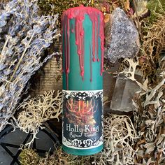 a candle with red and green drips on it sitting next to some dried plants