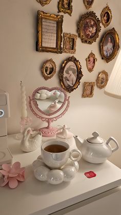 a white table topped with cups and saucers filled with liquid next to pictures on the wall