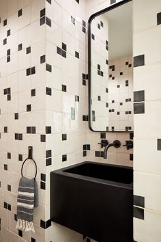 a bathroom with black and white tiles on the wall, sink and mirror in it