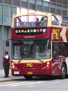 a red double decker bus driving down a street next to a tall building with lots of windows