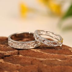 two white gold wedding rings sitting on top of a stone slab with flowers in the background