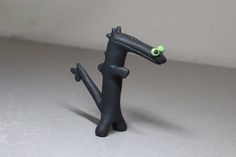 a black toy with green eyes on it's head and legs, sitting on a white surface