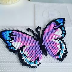 a close up of a butterfly made out of plastic beads on a table with a vase in the background