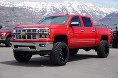 a red truck parked in a parking lot with mountains in the background