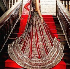 a woman in a red and gold bridal gown standing on the stairs with her hands on her hips