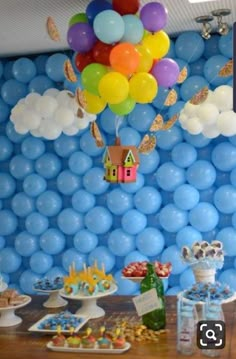 a table topped with lots of balloons and cupcakes next to a wall covered in clouds