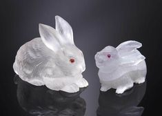 two glass rabbits sitting next to each other on top of a black surface with red eyes