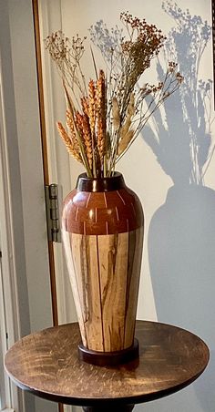 a vase sitting on top of a table with dried flowers in front of the wall