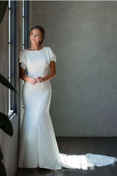 a woman in a white dress leaning against a wall