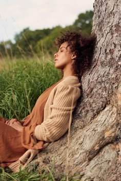 a woman is sitting on the ground next to a tree and has her eyes closed