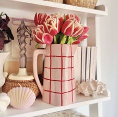 pink flowers in a vase on top of a white shelf next to books and shells