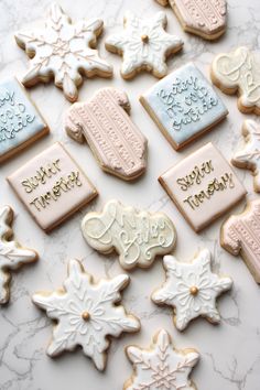 decorated cookies are arranged on a marble countertop with writing and snowflakes