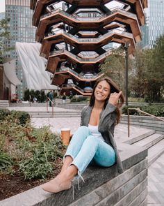 a woman sitting on top of a stone wall next to a tall building with a wooden structure in the background