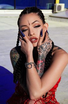 a woman with tattoos and piercings on her face is sitting in front of a building