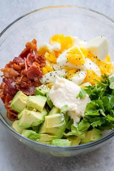 a glass bowl filled with eggs, avocado, bacon and other food items