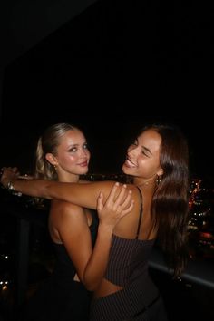 two beautiful young women standing next to each other in front of a city at night