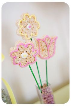 three crocheted flowers in a vase with pink and yellow yarn on the stems