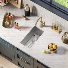 a kitchen sink sitting under a window next to a counter top with bowls of fruit on it