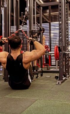 a man sitting on the ground in front of a gym machine with his back to the camera