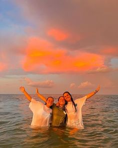 two women are standing in the water with their arms up and smiling at the camera