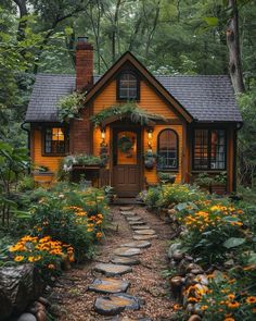 a small yellow house in the woods with flowers and plants around it's front door