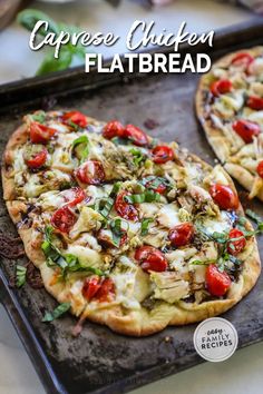 two flatbread pizzas with tomatoes and basil on top, sitting on a baking sheet