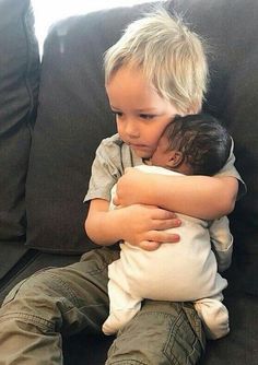 a little boy sitting on top of a couch hugging another child's head with both hands