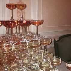 a table topped with lots of wine glasses next to a black chair and white wall