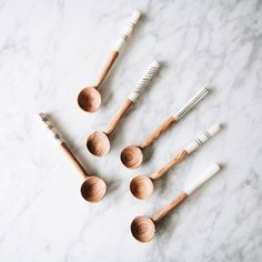 six wooden spoons with white handles on a marble countertop next to toothbrushes