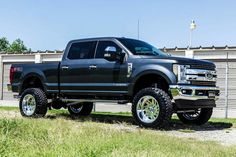 a large black truck parked on top of a grass covered field next to a building