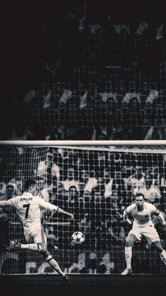 two men playing soccer in front of a goal with people watching from the sidelines